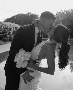 a bride and groom kissing in front of a pond at their wedding reception, black and white photograph