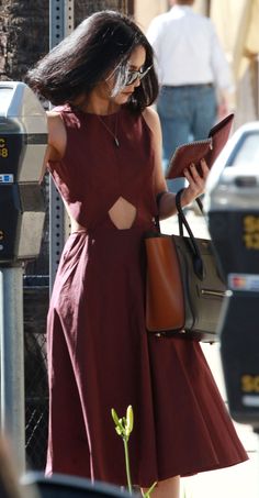 a woman in a red dress is looking at her cell phone while standing next to a parking meter