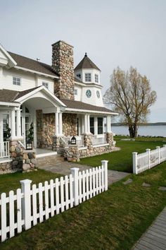 a white picket fence in front of a large house with a stone chimney on the corner