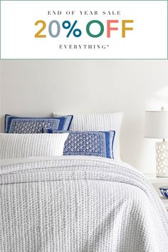 a bed with white sheets and blue pillows on it, next to a wall that says end of year sale 20 % off everything