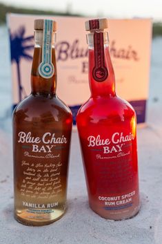 two bottles of blue chair bay are sitting next to each other on the sand in front of a box