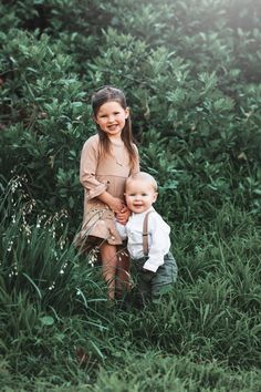 two young children standing in tall grass with one holding the other's head and smiling