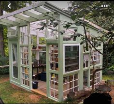 a small green house sitting in the middle of a yard with lots of windows on it