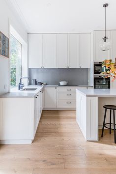 a large kitchen with white cabinets and wooden flooring, along with an island in the middle