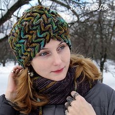 a woman wearing a knitted hat and scarf in the snow with her hand on her ear