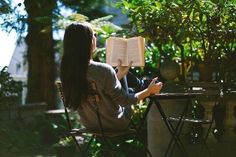 a woman sitting at a table with an open book in her lap and reading it