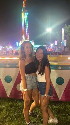 two young women standing next to each other in front of a carnival ride at night