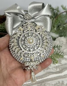 a hand holding a silver ornament with a bow on it's head