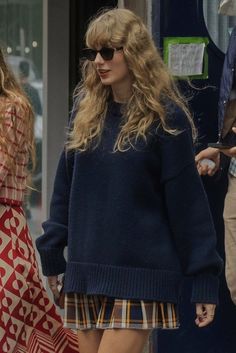 a woman walking down the street wearing a blue sweater and plaid skirt