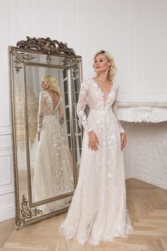 a woman standing in front of a mirror wearing a wedding dress with long sleeves and an open back