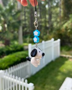 a hand holding a keychain with a dog on it's side and a white picket fence in the background