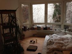 an unmade bed sitting in front of two windows next to a bookshelf