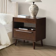 a nightstand with a lamp on top of it next to a bed