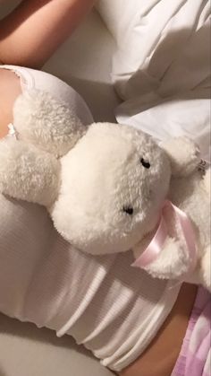 a white teddy bear laying on top of a woman's stomach with her arm wrapped around it