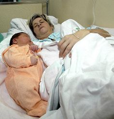 a woman laying in a hospital bed next to a sleeping baby with an oxygen tube