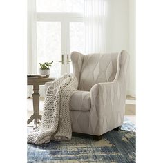 a chair with a blanket on top of it in front of a window and a table