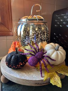 some fake pumpkins are sitting on a table next to a glass jar with spider decorations