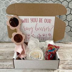 a box with some items inside it on a wooden table next to a sign that says will you be our ring bearer?