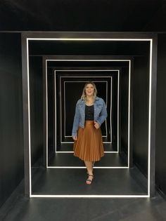 a woman standing in front of a black and white wall with multiple square shaped mirrors