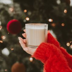 a woman holding a glass of milk in front of a christmas tree