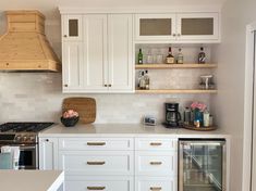 a kitchen with white cabinets and wooden shelves on the wall, along with a stainless steel range hood