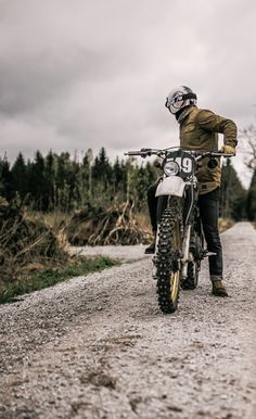 a man riding on the back of a motorcycle down a dirt road next to a forest