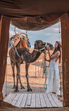 a woman standing next to a camel on top of a wooden platform in the desert