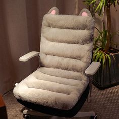 an office chair with a cat pillow on it's back and feet rest in front of a potted plant