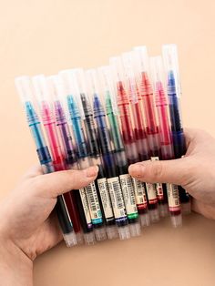 a person holding several different colored pens in their hands, with one hand on the other