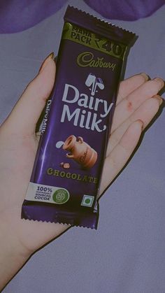 a person holding a bar of dairy milk chocolate in their left hand, on a bed