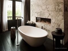 a large white bath tub sitting next to a fire place in a bathroom under a window