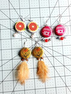 four different colored badges are hanging on a white tile wall next to some orange feathers