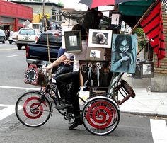 a man riding on the back of a bike down a street next to an umbrella