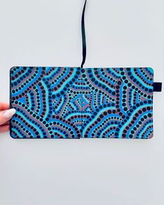 a hand holding a blue and black case with an intricate design on the front side