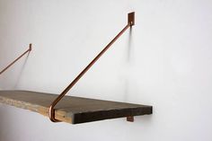 a wooden shelf with two metal hooks on it's sides and a white wall in the background