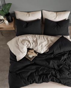 an unmade bed with black and white comforter on it, next to a plant