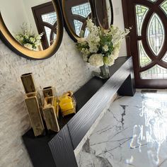 two mirrors on the wall above a mantle with vases and flowers in front of it