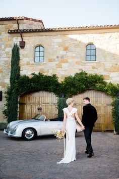 a bride and groom standing in front of a car