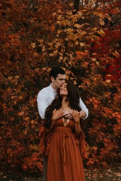 a man and woman standing next to each other in front of trees with orange leaves