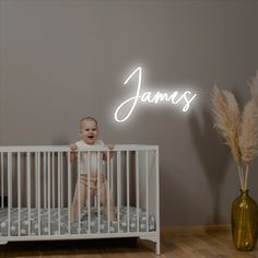 a baby standing in a white crib next to a wall with the name james written on it