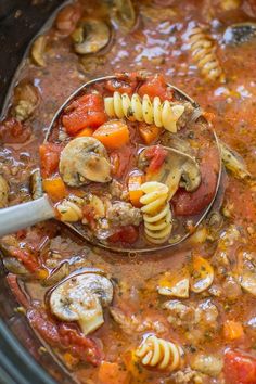 a ladle full of pasta and mushrooms in a slow cooker filled with soup