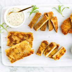 several pieces of breaded food on a white tray with dipping sauces and herbs