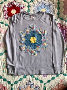 an image of a shirt that is laying on the bed with it's flower appliqued