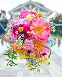 a person holding a bouquet of flowers in front of a building with water behind it