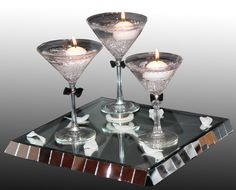 three martini glasses sitting on top of a glass table with candles in the middle and some napkins next to them