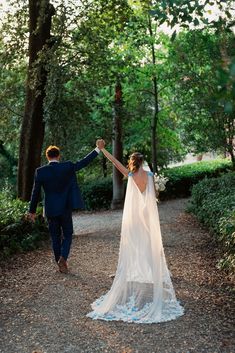 a bride and groom walking down a path holding hands