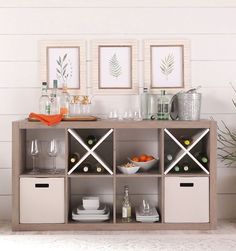 an open shelf with wine glasses, plates and bowls on it in front of two framed pictures