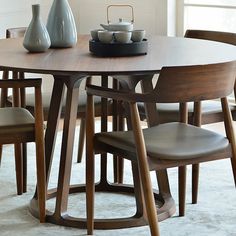 a wooden table with four chairs around it and a vase on the table next to it