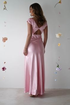 a woman in a long pink dress looking back at the wall with flowers on it