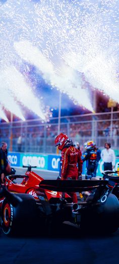 a man driving a red race car on top of a track with fireworks in the air